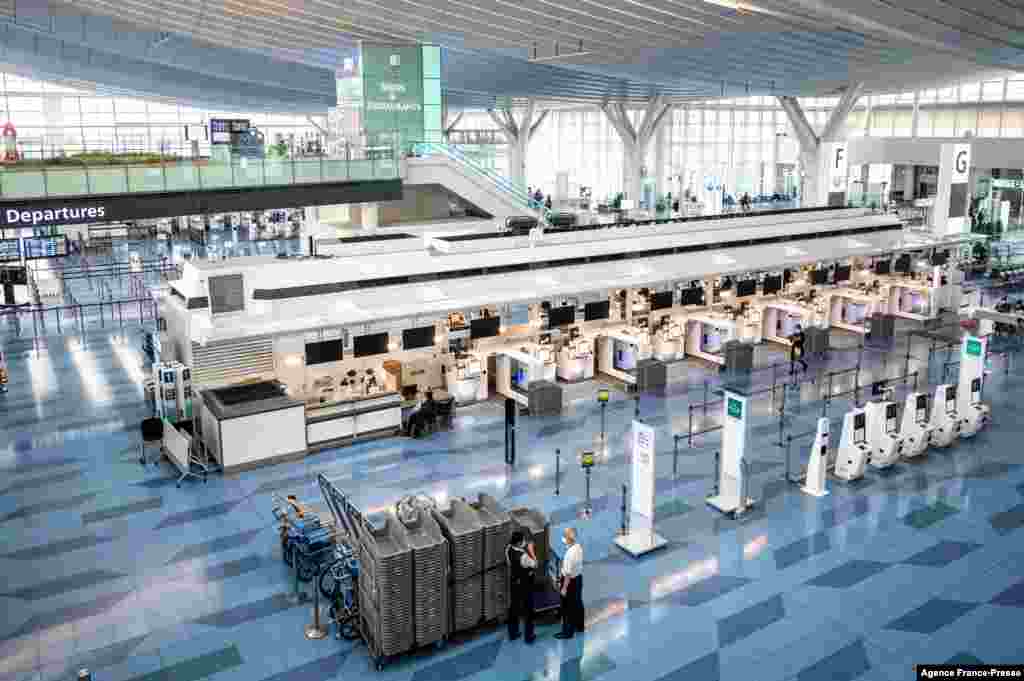 Staff members stand by in a mostly empty departures hall at Tokyo's Haneda international airport. More than 370,000 people are in left in limbo by Japan's coronavirus border rules, which bar almost all new arrivals.