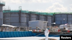 FILE - A worker, wearing protective suits and masks, takes notes in front of storage tanks for radioactive water at Tokyo Electric Power Co's (TEPCO) tsunami-crippled Fukushima Daiichi nuclear power plant in Okuma town, Fukushima prefecture, Japan, Feb.10, 2016.