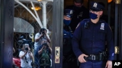 New York City police officers walk out of the apartment building where former New York Mayor Rudy Giuliani resides as members of the media observe, April 28, 2021.