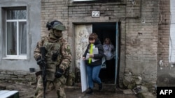 Російський військовослужбовець зі зброєю в руках супроводжує членів виборчої дільниці, відвідуючи виборців для голосування вдома. STRINGER/AFP