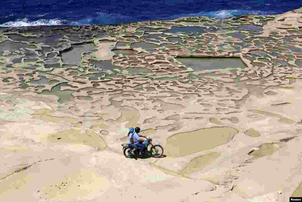 A man and his passenger ride a motorcycle near salt pans, believed to have been used for harvesting sea salt since Roman times, outside the village of Marsalforn, on the northern coast of the Maltese island of Gozo, June 12, 2013.