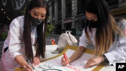Dr. Michelle Lee, left, a radiology resident, and Ida Chen, right, a physician assistant student, prepare posters they carry at rallies protesting anti-Asian hate, April 24, 2021, in New York's Chinatown.