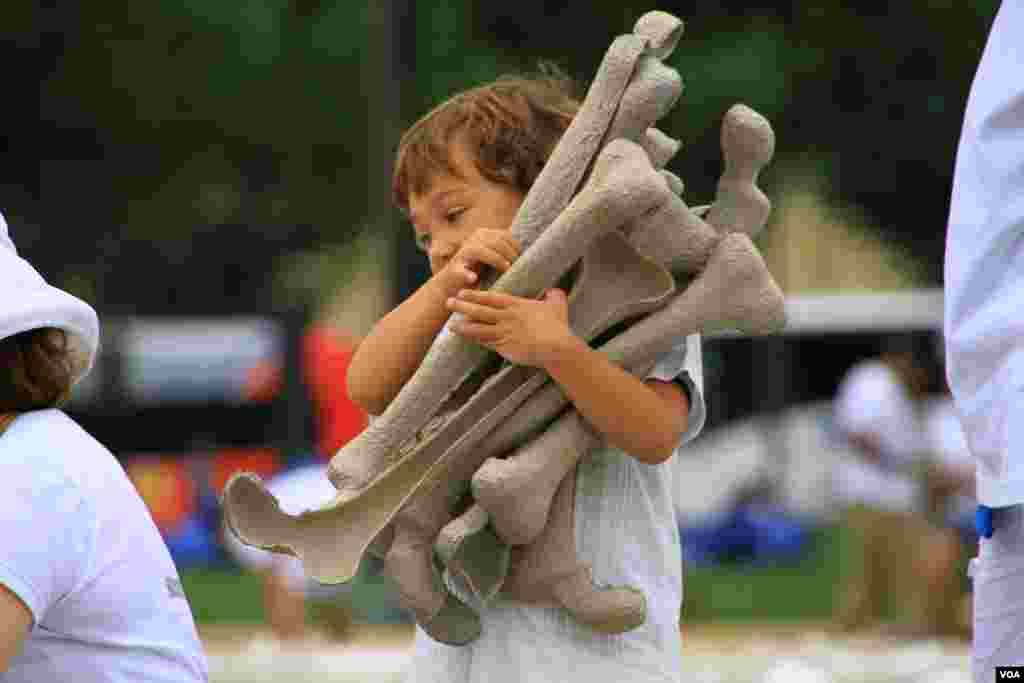 A child carries artificial bones for display at the "One Million Bones" installation on the National Mall, Washington, D.C, June 8, 2013. (Jill Craig/VOA)