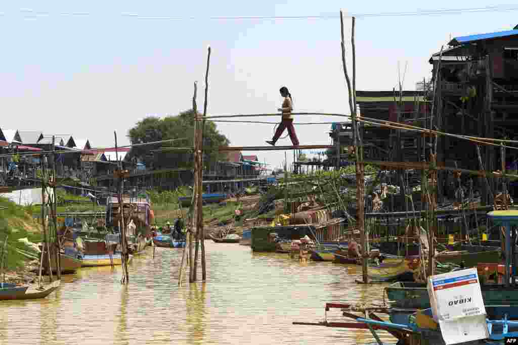 ស្រ្តីម្នាក់ឆ្លងកាត់ស្ពានឬស្សីលើអូរមួយក្នុងឃុំកំពង់ភ្លុកក្នុងខេត្តសៀមរាបប្រទេសកម្ពុជា។