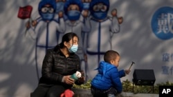 在北京前門街道的一幅抗疫宣傳畫下，一名幼兒在一名女子的看顧下玩耍。 （2021年11月17日）