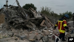 A rescue worker walks past a wrecked car on a site where several houses were destroyed after a Russian attack at a residential area in Zaporizhzhia, Ukraine, Oct. 9, 2022. 