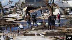 Gente de pie en el puente destruido a Pine Island mientras contemplan los daños causados por el huracán Ian en Matlacha, Florida, el domingo 2 de octubre de 2022. El único puente a la isla estaba muy dañado y sólo se podía acceder por mar o aire. (AP Foto/Gerald Herbert)