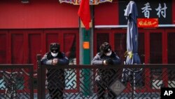 In this Feb. 23, 2020, photo, security guards wearing protective face masks browse their smartphones near shuttered business shops in Beijing.