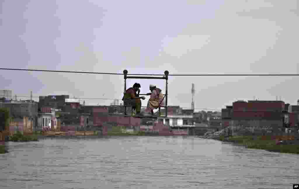 Two Pakistani men chat while crossing a stream that divides a neighborhood, using a rope-operated bridge, on the outskirts of Islamabad.
