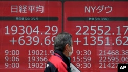 A man walks past an electronic stock board showing Japan's Nikkei 225 and New York Dow index at a securities firm in Tokyo Friday, March 27, 2020. Shares are mostly higher in Asia after stocks surged again on Wall Street with the approaching…