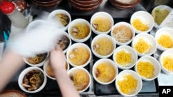 A staff member prepares small bowls of noodles for participants of Tokyo Ramen Tours at Shinbusakiya, a ramen shop that offers "Hokkaido classics," at Shibuya district on April 2, 2024, in Tokyo. (AP Photo/Eugene Hoshiko)