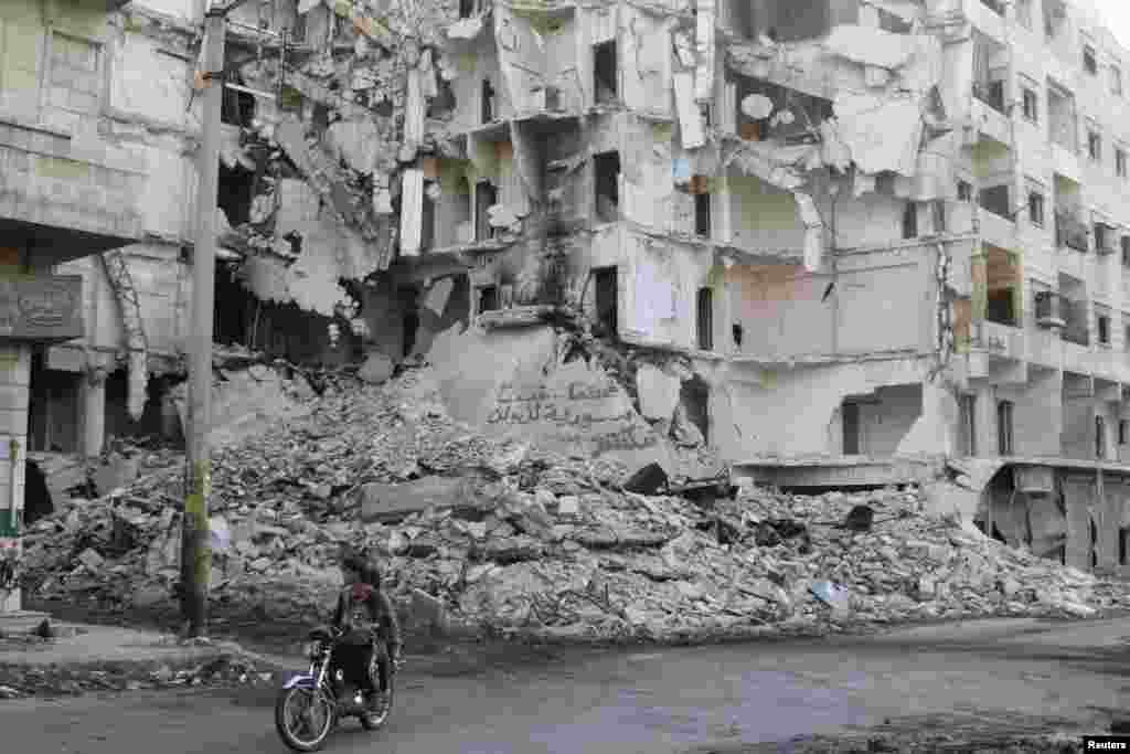 Dua pria mengendarai sepeda motor melewati gedung-gedung yang hancur di distrik Bustan al-Basha, kota Aleppo, Suriah. 