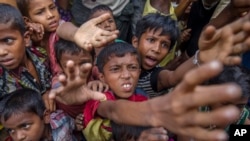 Rohingya Muslim children, who crossed over from Myanmar into Bangladesh, stretch out their arms out to collect chocolates and milk distributed by Bangladeshi men at Taiy Khali refugee camp, Bangladesh, Sept. 21, 2017.
