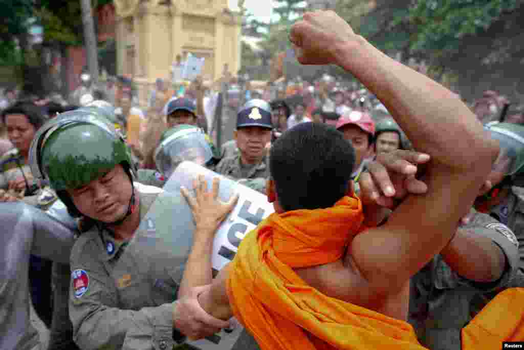 Polisi anti-huru hara melindungi seorang pria yang dituduh berusaha memukul biarawan Buddha, dalam protes melawan kecurangan dalam pemilihan umum di Phnom Penh (28/7).