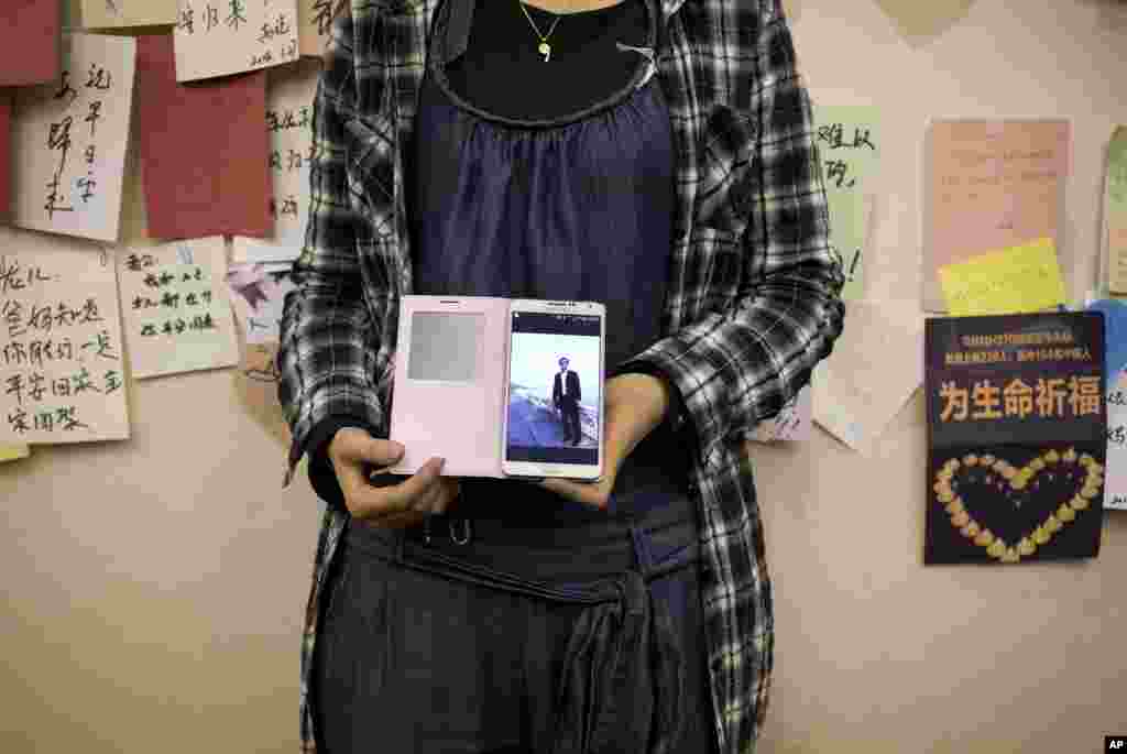 The daughter of a Chinese passenger on Flight MH370 shows her mobile phone displaying a photo of her father, near the wall displaying messages of wishes for the passengers at a hotel in Beijing, April 11, 2014.