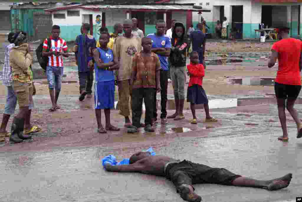 People gather around a man, suspected of dying from the Ebola virus, in one of the main streets on the outskirts of the city center of Monrovia, Liberia, Aug. 26, 2014.