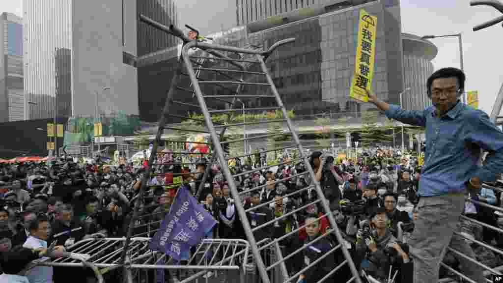 A pro-democracy protester stands on barricades to raise a sign that reads "I want genuine universal suffrage" while workers start clearing away barricades at an occupied area outside government headquarters in Hong Kong, Nov. 18, 2014.