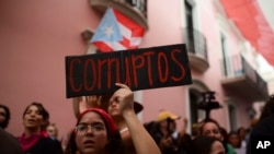 Una joven sostiene un letrero que dice en español "Corrupto" mientras protestaba frente a la mansión ejecutiva conocida como La Fortaleza, en el Viejo San Juan, exigiendo la renuncia del gobernador Wanda Vázquez después del descubrimiento de un viejo alma