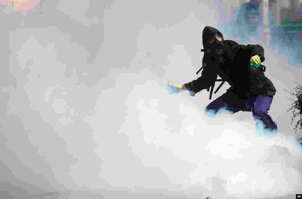 An anti-government protester gets ready to throw back a tear gas canister fired by riot police in Bangkok.