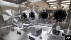 Ryan Zeigler, Apollo sample curator, left, stands next to a nitrogen-filled case displaying various lunar samples collected during Apollo missions, inside the lunar lab at the NASA Johnson Space Center, June 17, 2019, in Houston, Texas.