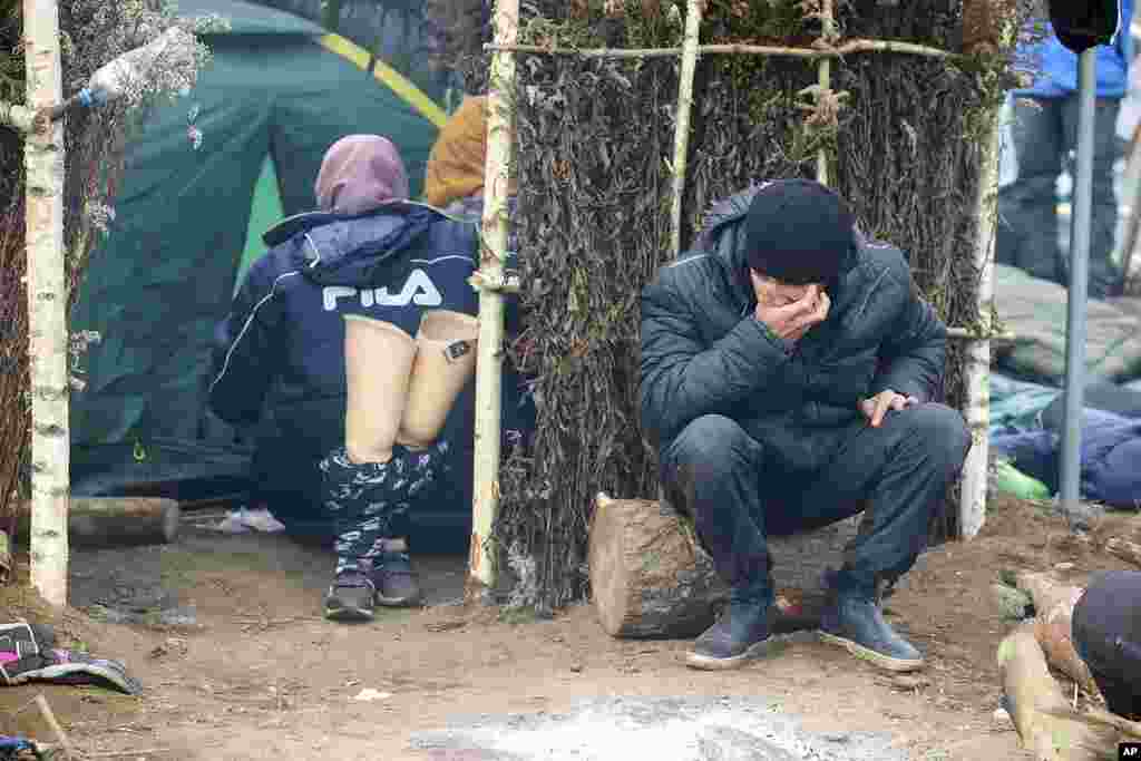 A man sits outside a tent as other migrants gather at the Belarus-Poland border near Grodno, Belarus. About 15,000 Polish troops have joined riot police and guards at the border. The Belarusian Defense Ministry accused Poland of an "unprecedented" military buildup there, saying that migration control didn't warrant such a force. 