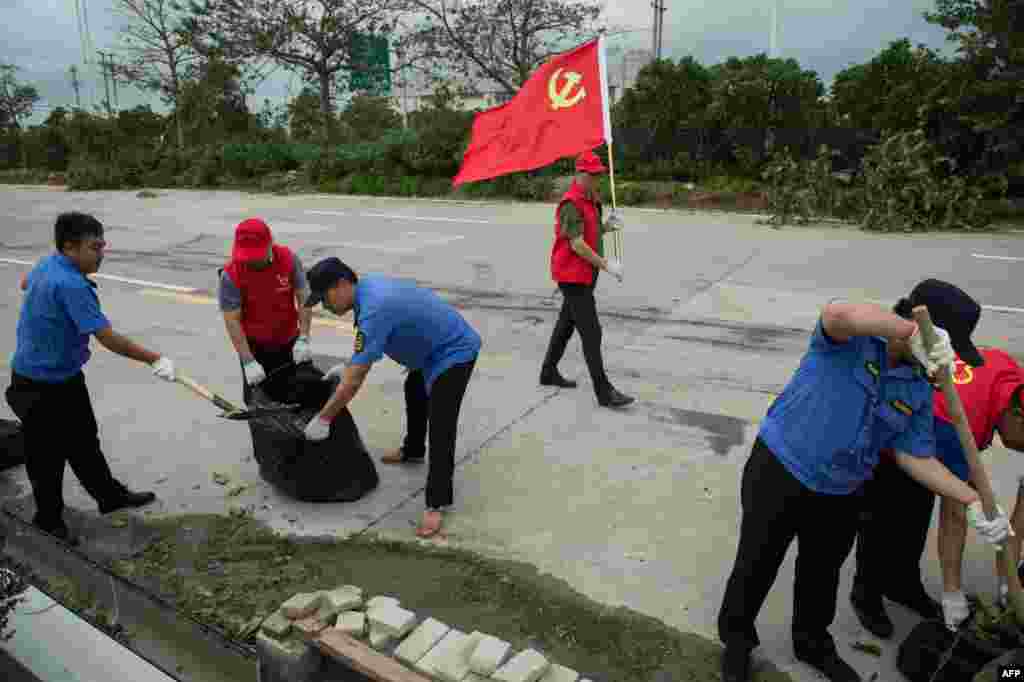 2018年9月17日,中国广东省珠海,台风山竹过后,志愿者和警察清理高速公路上的碎片,一名男子手持中国共产党的旗帜,警示过往车辆。台风山竹造成海水倒灌,樹木倒伏,但据说抗灾清理工作比较迅速。