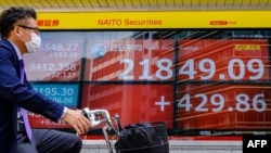 A cyclist wearing a face mask rides past an electric quotation board displaying the morning numbers of the Nikkei 225 Index on the Tokyo Stock Exchange in Tokyo on May 28, 2020. (Photo by Philip FONG / AFP)