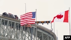 Bendera Amerika Serikat dan Kanada berkibar di dekat Jembatan Bluewater, yang melintasi Sungai St. Clair, perbatasan antara Sarnia, Ontario dan Port Huron, Michigan, 29 Januari 2025. (Geoff Robins/AFP)