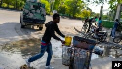 Un vendedor ambulante empuja su carrito frente al Palacio Nacional mientras un coche de policía blindado patrulla la zona, en Puerto Príncipe, Haití, el martes 23 de abril de 2024.