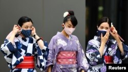 Women in traditional costumes, wearing protective face masks, walk outside the National Stadium, the main venue of the Tokyo 2020 Olympic Games, in Tokyo, Japan, Aug. 3, 2021.