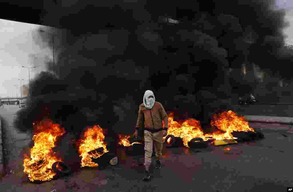 A protester passes burning tires along a main highway that leads to Beirut's international airport during a protest against the increasing prices of consumer goods and the crash of the local currency in Beirut, Lebanon.