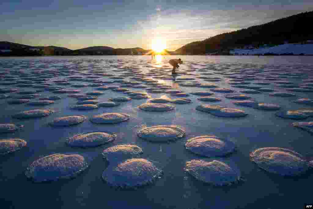 A skater observes pancakes snow on the frozen Lake des Rousses in Les Rousses, central-eastern France, Jan. 1, 2025. This phenomenon forms when slushy ice in water clumps into round, pancake-like shapes due to waves or currents.