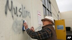 FILE - Tom Garing cleans up racist graffiti painted on the side of a mosque in what officials are calling an apparent hate crime, Feb. 1, 2017, in Roseville, Calif. (AP Photo/Rich Pedroncelli) 