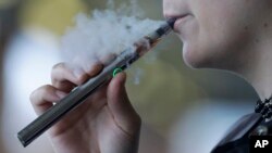 In this Oct. 4, 2019 photo, a woman using an electronic cigarette exhales in Mayfield Heights, Ohio. 