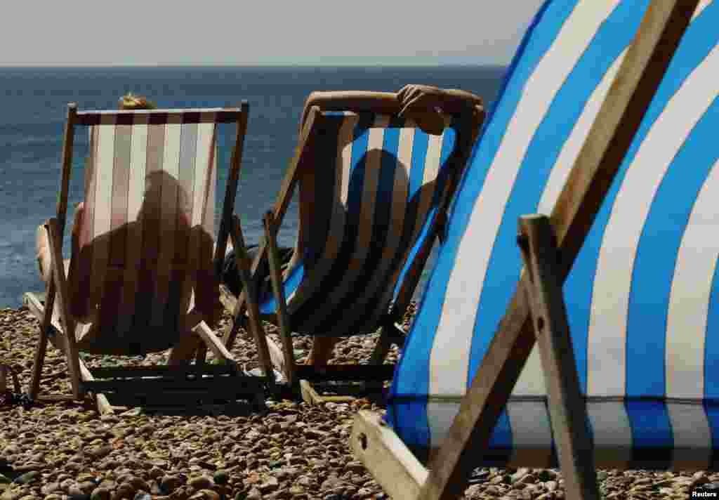 Dua orang duduk berjemur di pantai Brighton, Inggris Selatan. Gelombang panas berkepanjangan yang pertama kalinya dalam tujuh tahun di Inggris mengejutkan negara itu, dengan menekuknya rel-rel kereta, penjualan kipas angin-kipas angin listrik, dan perkiraan para ilmuwan yang mengatakan kenaikan suhu itu dapat berakibat kematian awal pada ratusan jiwa.