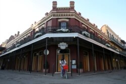 FILE - A man rides his bicycle in front of a boarded up French Quarter restaurant amid the outbreak of the coronavirus, in New Orleans, Louisiana, March 25, 2020.