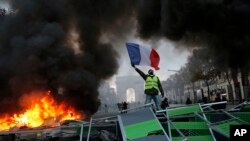 Seorang pengunjuk rasa melambaikan bendera Perancis ke arah barikade yang terbakar di depan Champs-Elysees, Paris. (24/11).