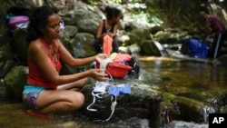 A woman washes her protective face masks with runoff water from the Avila mountain in Caracas, Venezuela, as water shortages have continued to deepen in the country at a time when the threat of the coronavirus makes washing hands even more critical.