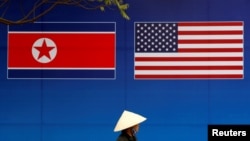 Seseorang berjalan melewati spanduk yang menunjukkan bendera Korea Utara dan AS di depan bendera Korea Utara-AS. KTT di Hanoi, Vietnam, 25 Februari 2019. (Foto: Reuters)