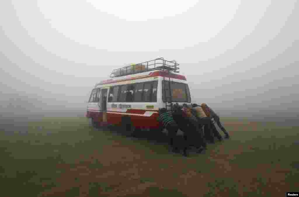 Para penumpang membantu mendorong bus yang mogok, pada suatu pagi yang dingin dan berkabut di kota Agartala, negara bagian Tripura, India.