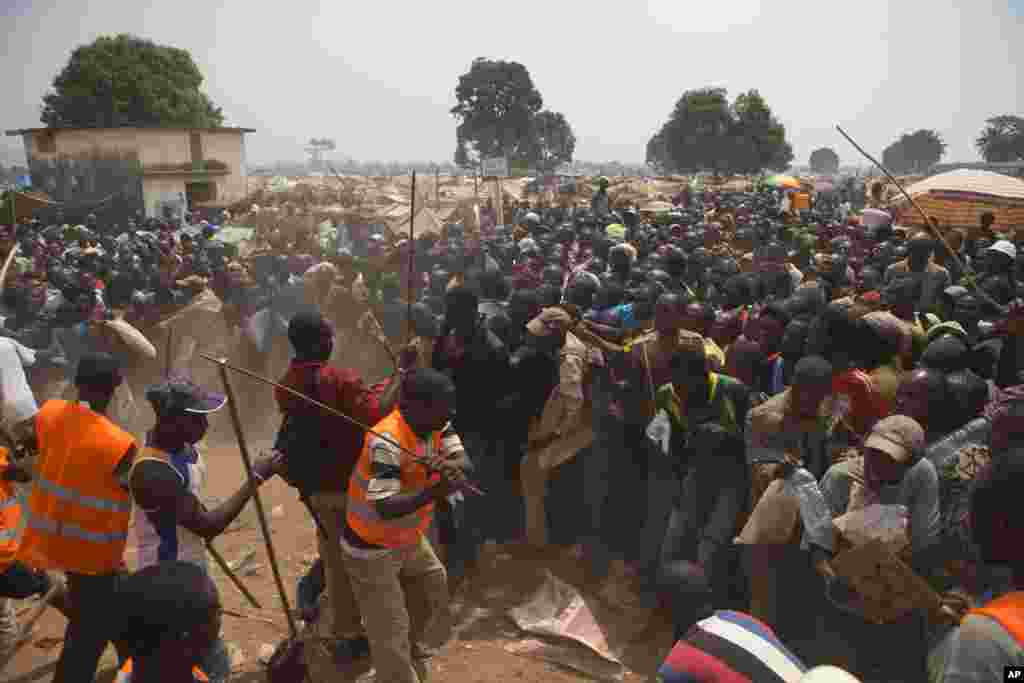 Volunteers use sticks to fend off the crowd trying to enter a food and supplies distribution point at a makeshift camp housing an estimated 100,000 displaced people, at Mpoko Airport, in Bangui, Central African Republic.