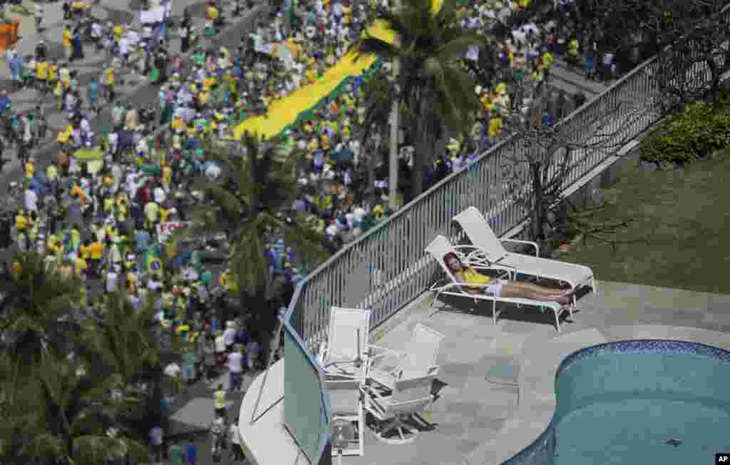 A woman sleeps in a residential penthouse while thousands below march in an anti-government protest demanding the impeachment of Brazil's President Dilma Rousseff, Copacabana Beach, Rio de Janeiro, Brazil, Aug. 16, 2015.
