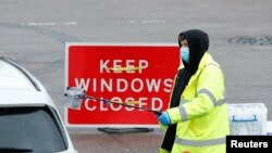 Seorang petugas NHS memberikan alat tes COVID-19 ke seorang pengemudi di pusat tes lantatur di tengah merebaknya wabah virus corona di Broxbourne, Hertfordshire, Inggris, 2 Februari 2021. 