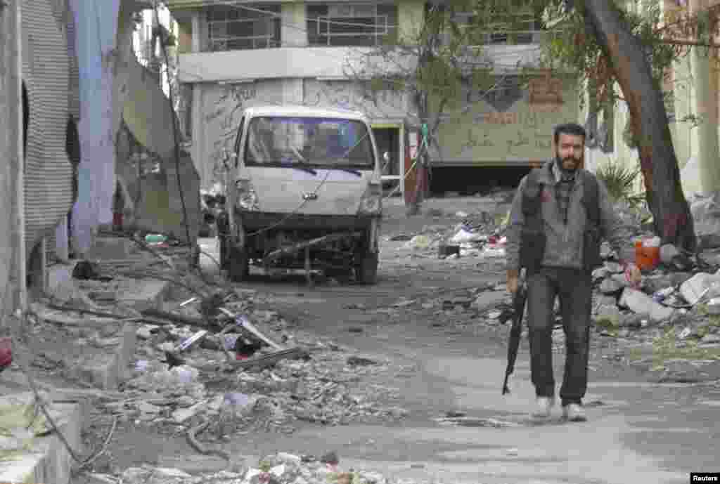 A Free Syrian Army fighter holds his weapon as he walks along a damaged street in the besieged area of Homs, Jan. 30, 2014.