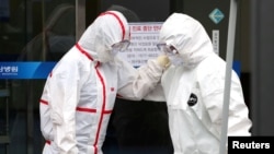 Medical workers wearing protective gears comfort each other outside a hospital in Daegu, South Korea, Feb. 28, 2020.