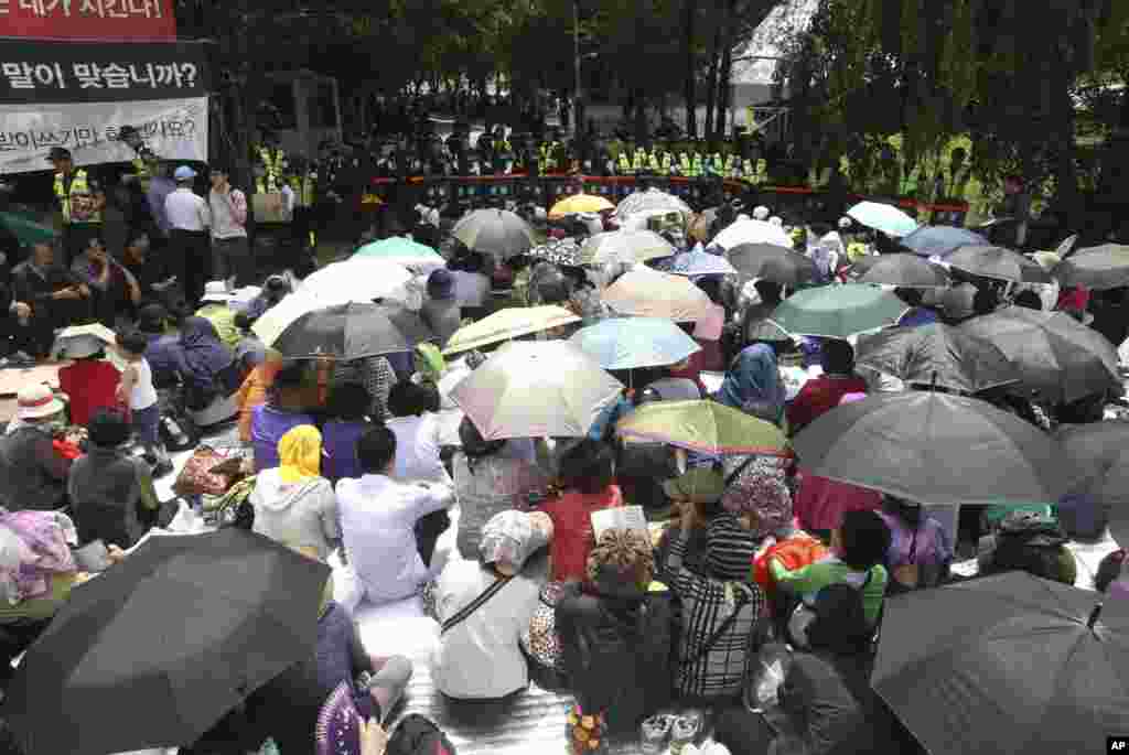 Evangelical Baptist Church believers sit as police officers searching for a fugitive billionaire businessman over April's ferry sinking stand in line in font of the main gate of the church in Anseong, South Korea, June 11, 2014.