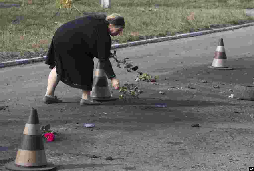 A woman puts flower on the ground in the spot where shell landed killing several people, on the outskirts of Mariupol, Ukraine, Oct. 15, 2014.