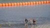 Migrantes caminan entre alambre de concertina y una serie de boyas colocadas en el agua a lo largo de la frontera de Río Grande con México para evitar la entrada de inmigrantes ilegales a EEUU en Eagle Pass, EEUU, el 16 de julio de 2023.