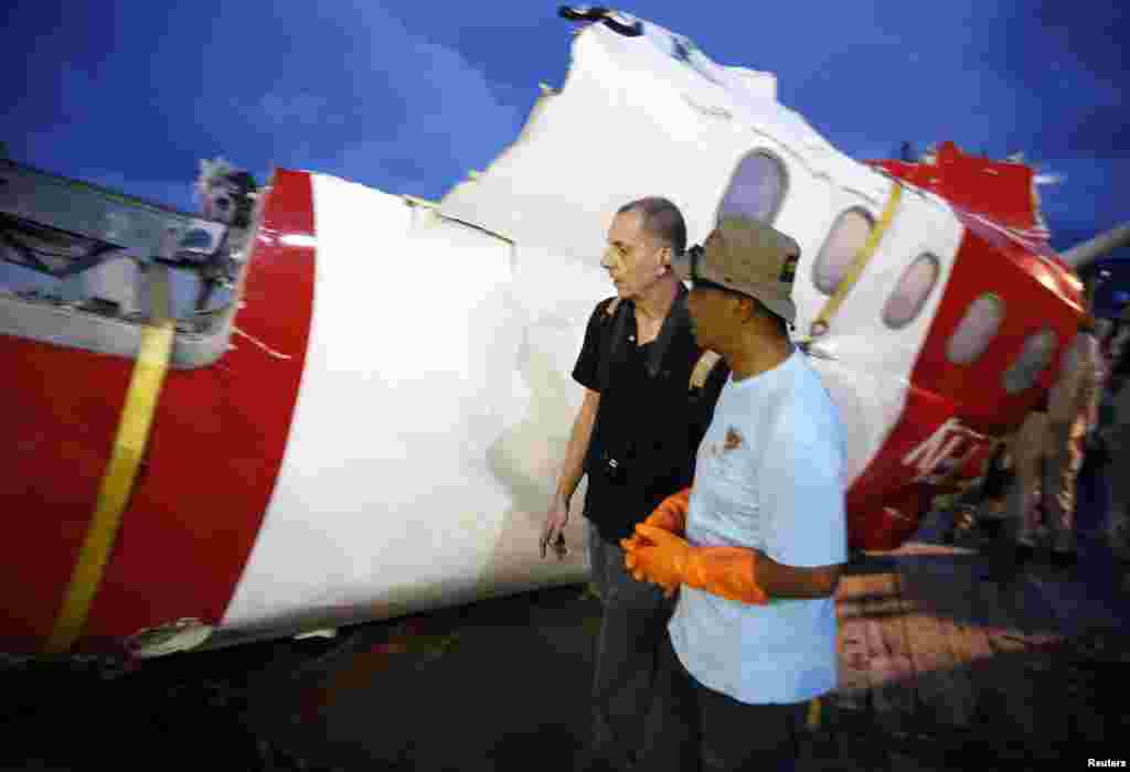 Investigators walk near a section of the tail of AirAsia Flight QZ8501 passenger plane in Kumai Port, near Pangkalan Bun, Central Kalimantan, Jan. 11, 2015.
