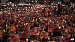 Protesters hold candles and signs during a rally denouncing Japanese Prime Minister Shinzo Abe and also demanding the South Korean government cancel its GSOMIA agreement with Japan, in downtown Seoul, South Korea, Aug. 15, 2019.